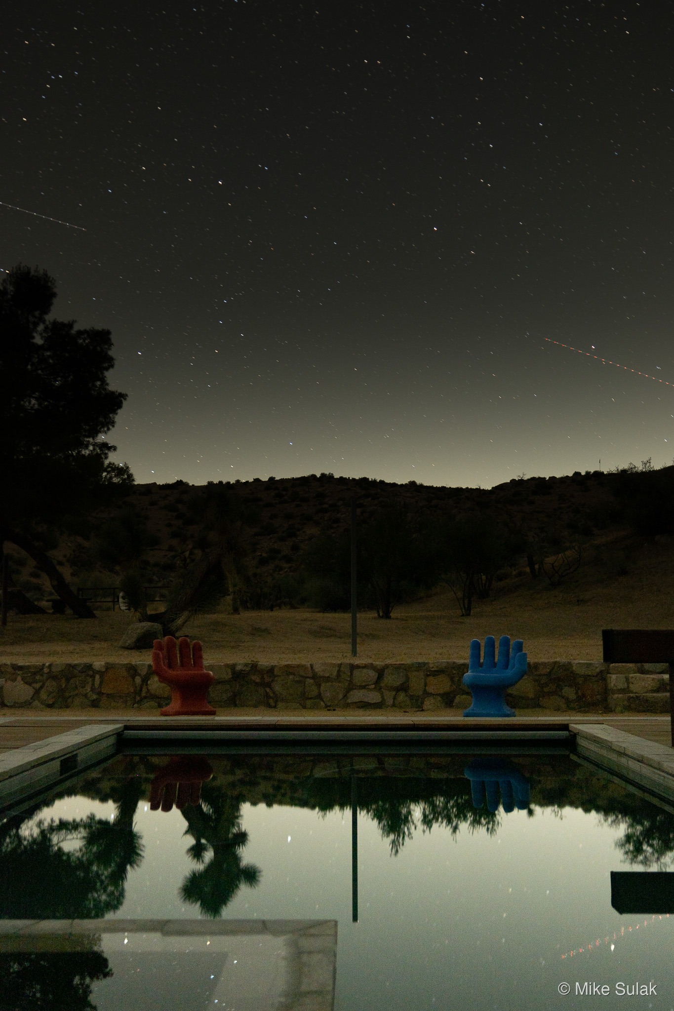 Pool at night with red and blue hand-shaped chairs, stars overhead